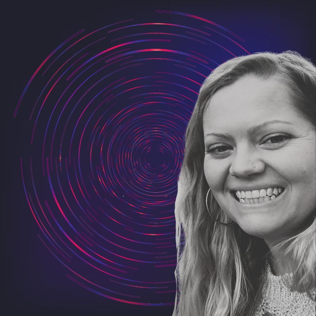 Jenna, in black and white, smiles to the camera. She is on a background of circles in red and blue.