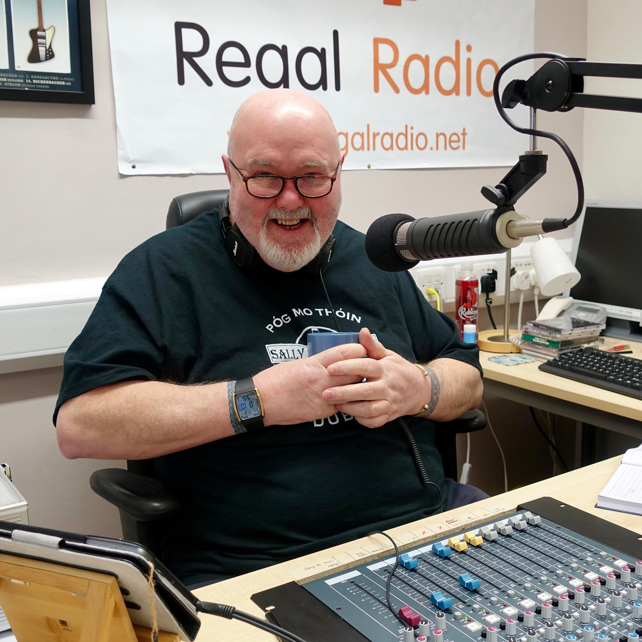 Mike sitting in the studio with headphones around his neck and holding a mug of tea.